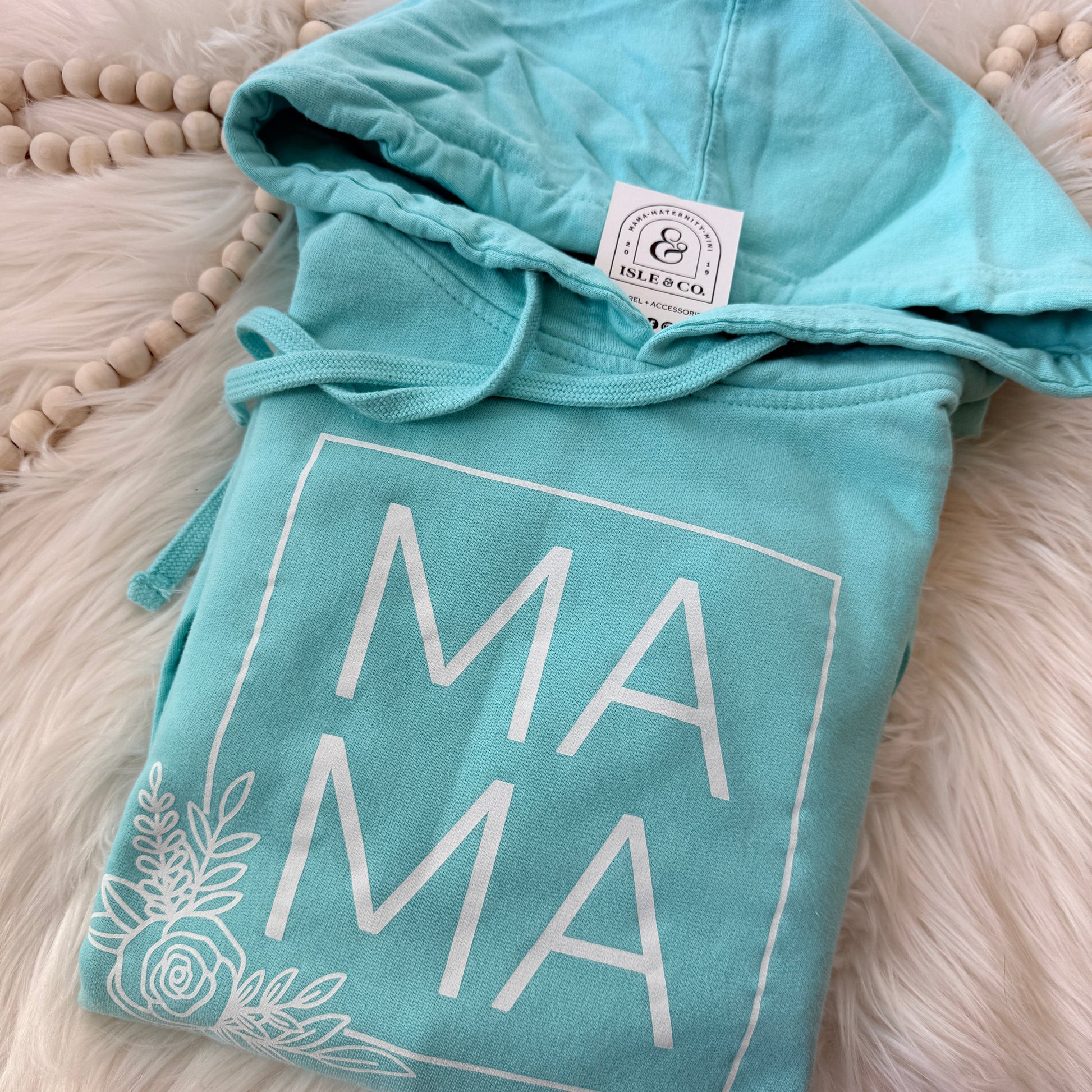 Teal hoodie with 'MAMA' text on a fluffy white surface