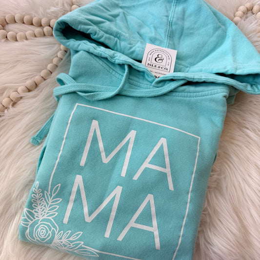 Teal hoodie with 'MAMA' text on a fluffy white surface