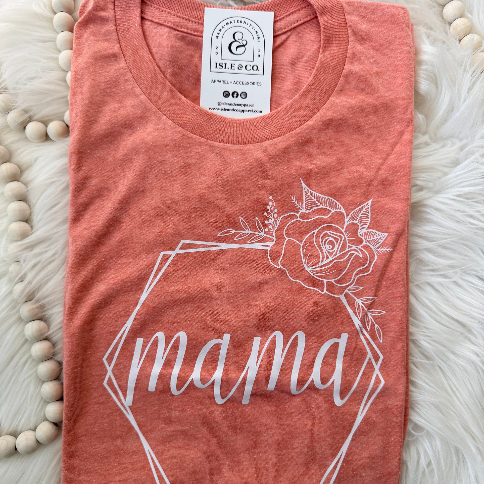 Pink t-shirt with floral design and 'mama' text on a fluffy white surface