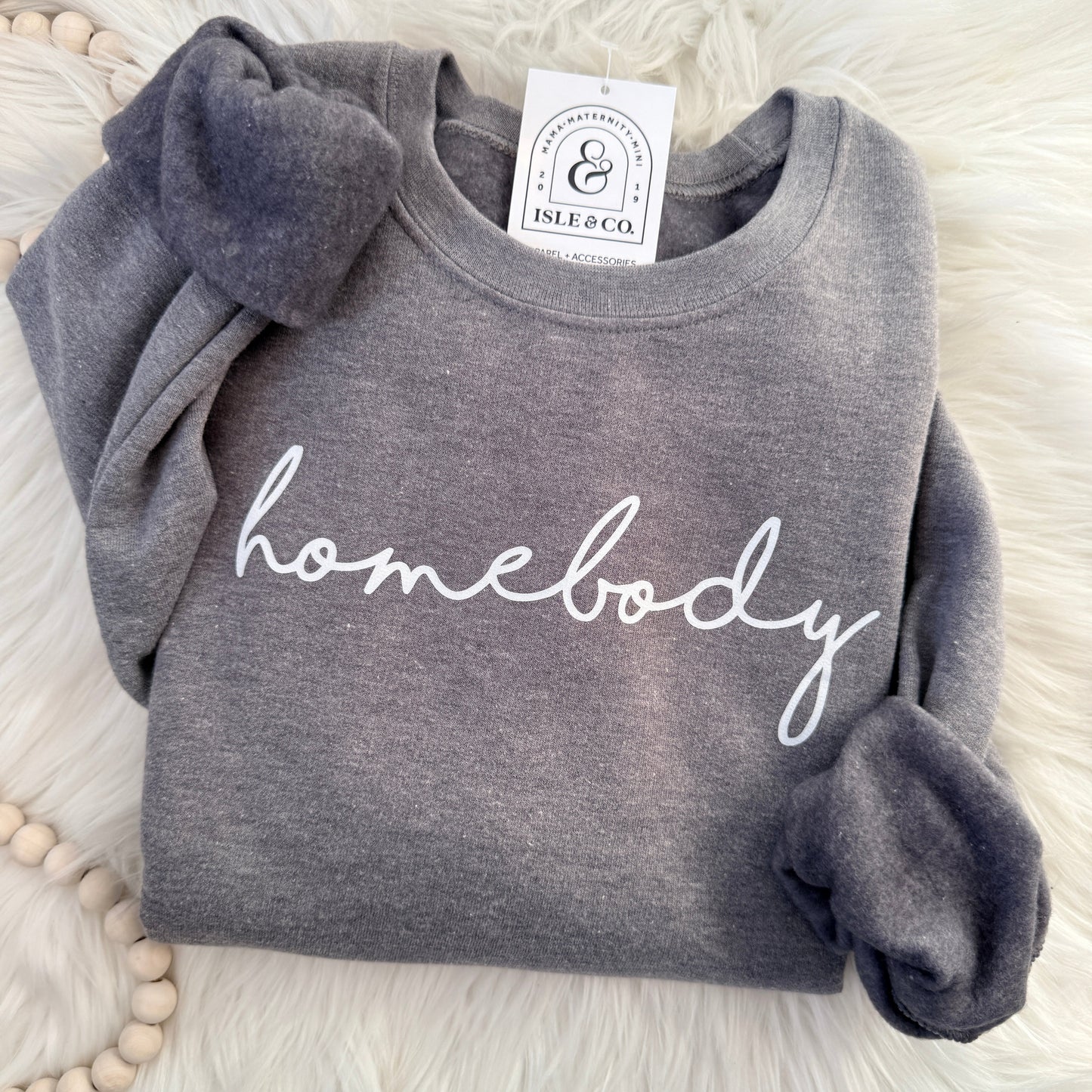 Gray sweatshirt with 'homebody' text on a white fluffy surface