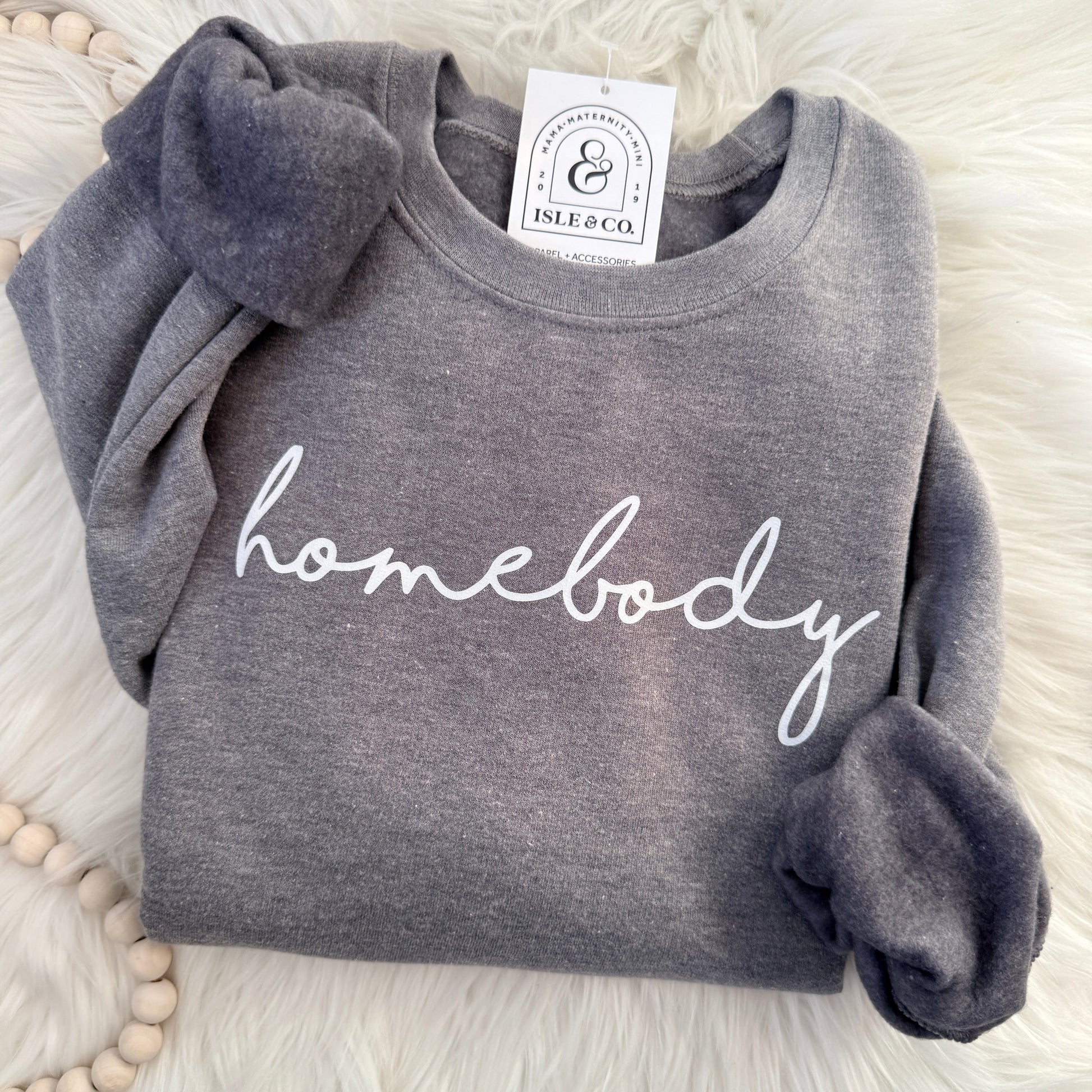 Gray sweatshirt with 'homebody' text on a white fluffy surface