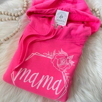 Pink hoodie with 'mama' and a rose design on a fluffy white surface