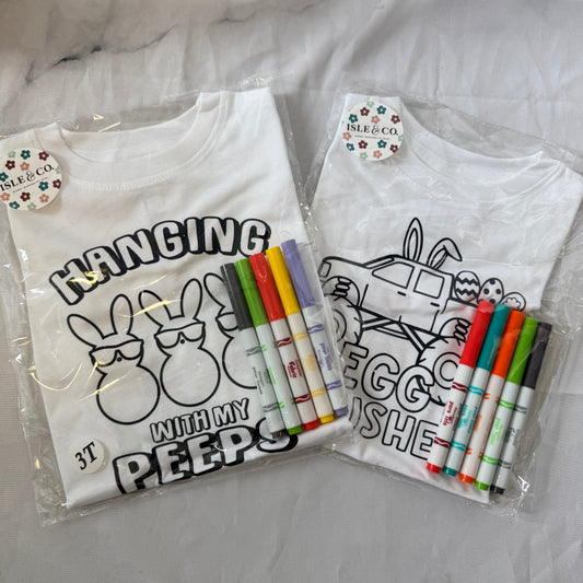 Two white t-shirts with black designs and markers on a white background