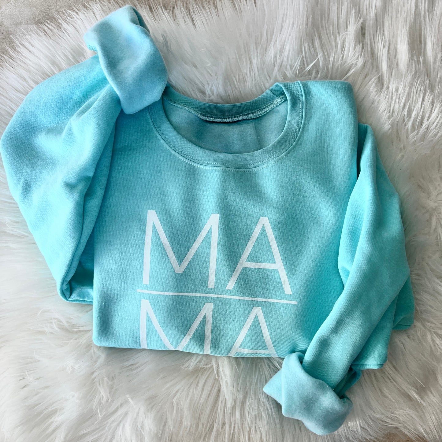 Light blue sweatshirt with 'MAMA' print on a fluffy white surface